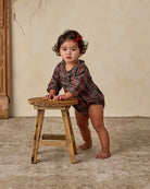 Child in a red plaid romper with a ruffled collar