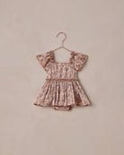 Floral baby romper on a hanger against a beige background