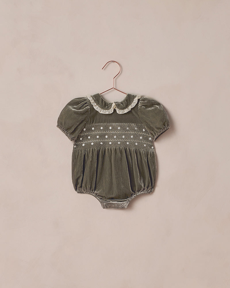 Green baby romper with lace collar on a beige background