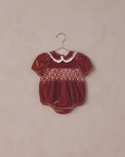 Red baby romper with white collar on a beige background