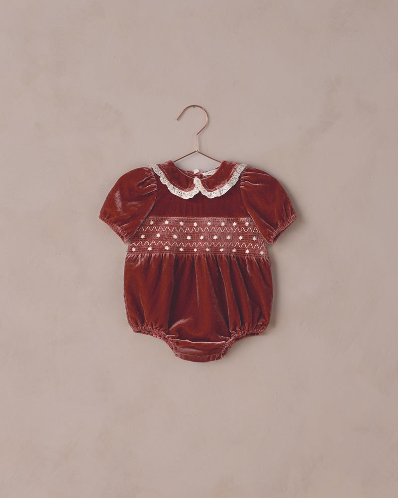 Red baby romper with white collar on a beige background