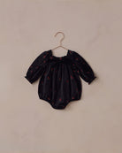 Black baby romper with a red floral pattern on a beige hanger against a beige background