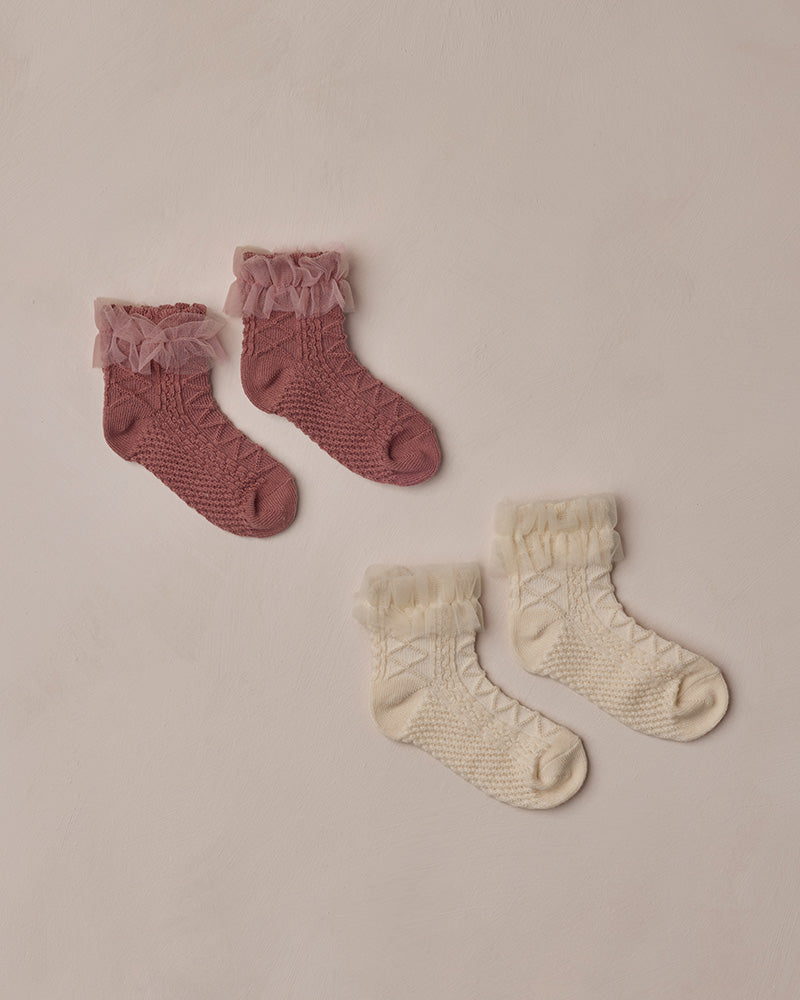 Two pairs of baby socks, one pink and one beige, on a beige background.