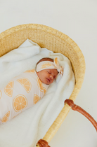 baby swaddled in orange fruit print swaddle blanket with matching headband 