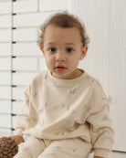 An off-white long-sleeve baby sweatshirt with a repeating pattern of small deer and pine trees in muted gray and beige, shown against a plain white background.