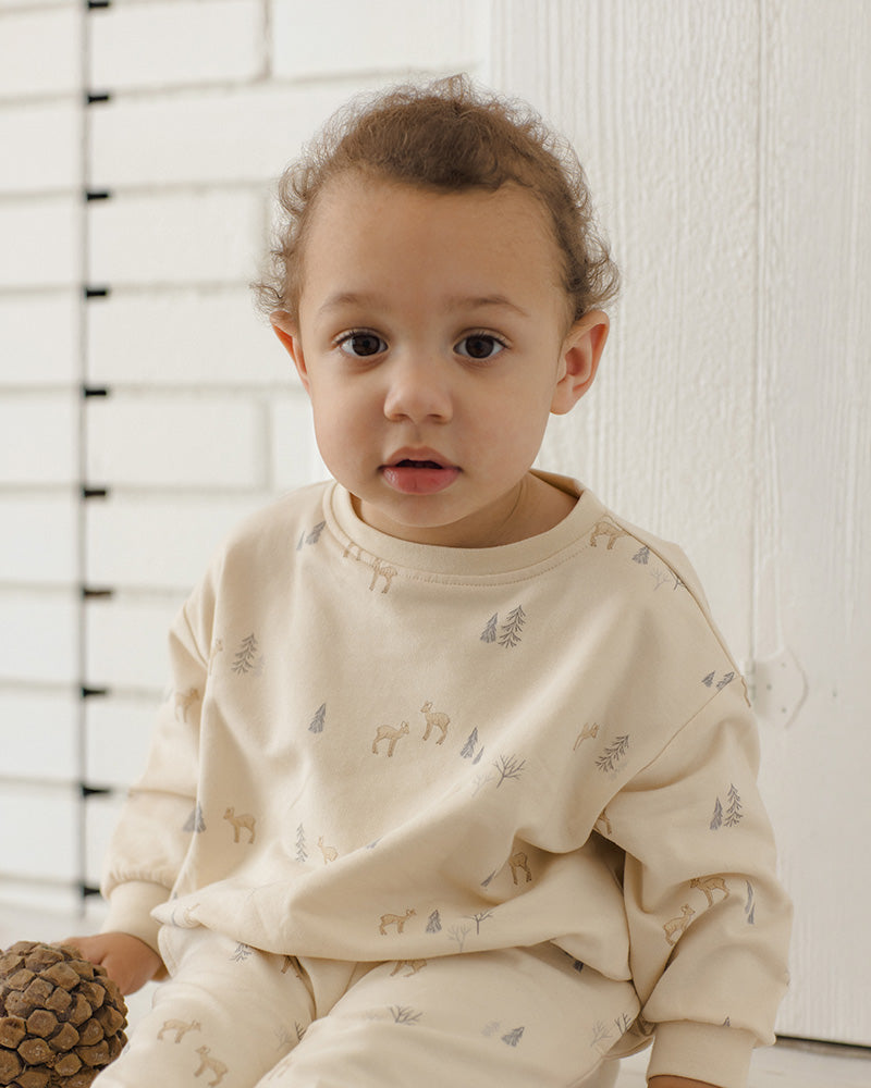 An off-white long-sleeve baby sweatshirt with a repeating pattern of small deer and pine trees in muted gray and beige, shown against a plain white background.