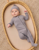 A baby wearing a solid gray long-sleeve footed sleeper and matching hat.