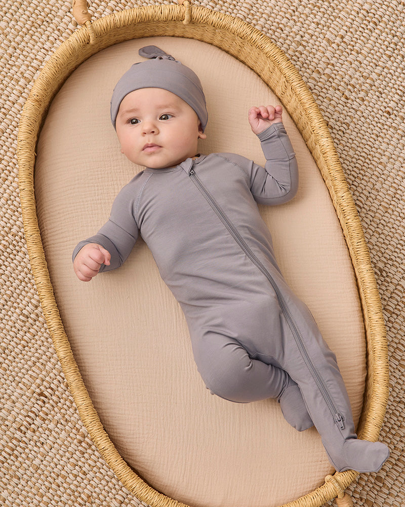 A baby wearing a solid gray long-sleeve footed sleeper and matching hat.