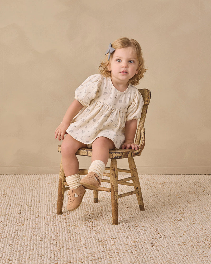 A baby girl's short-sleeve dress in cream cotton fabric with a delicate gray floral print, featuring a smocked bodice and puffed sleeves.