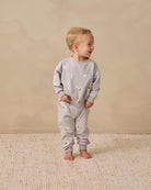 Light gray baby jogger pants with a celestial print of crescent moons, stars, and clouds, featuring an elastic waistband with drawstrings and ribbed ankle cuffs.
