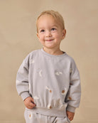 A light gray long-sleeve sweatshirt for toddlers, featuring an all-over celestial print of white clouds, crescent moons, and brown stars.