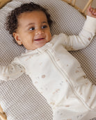 Baby lying on a textured surface wearing a white outfit with small farm patterns.