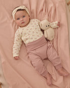 Baby lying on a pink blanket wearing a floral onesie and pink pants.