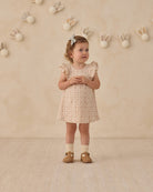 Young girl in a floral dress standing against a beige wall with decorative bunny rabbits.