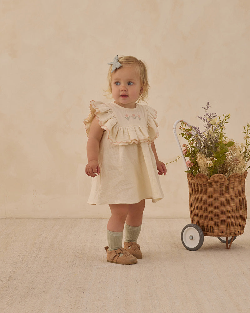 Young girl in a beige dress with floral detailing on the front. 