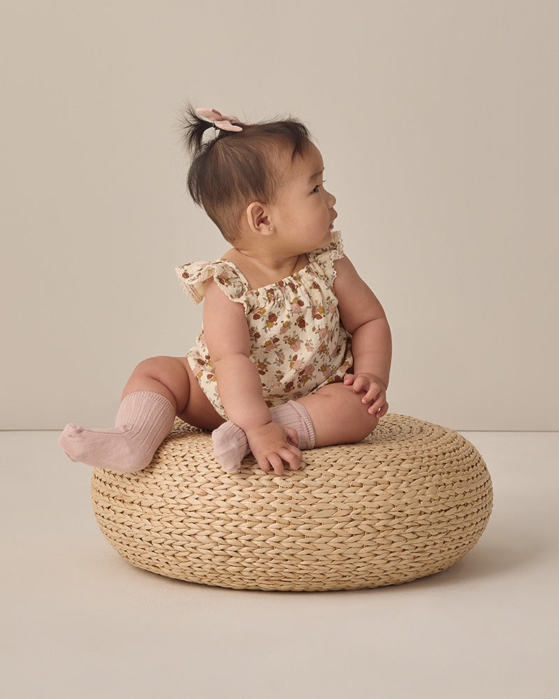 Baby sitting on a woven stool against a plain background