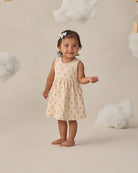 Young child in a beige dress and floral patterns on a white background