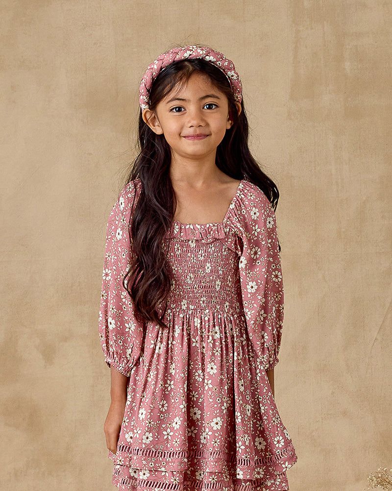 Young girl wearing a pink floral dress and headband against a beige background