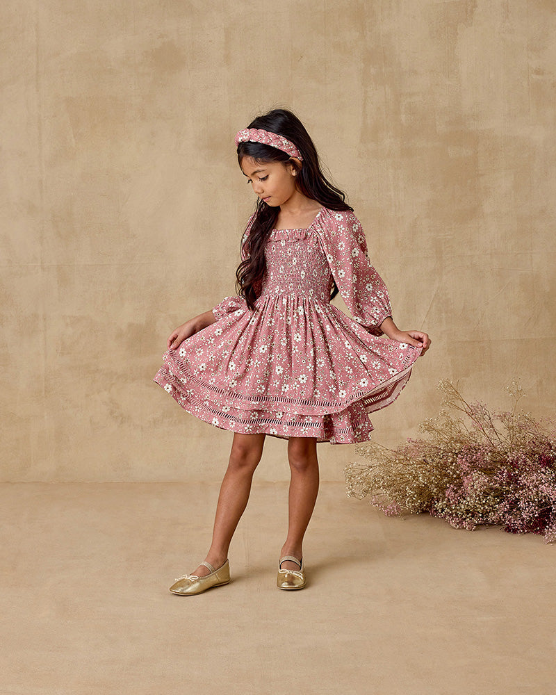 Young girl in a pink floral dress standing against a beige background