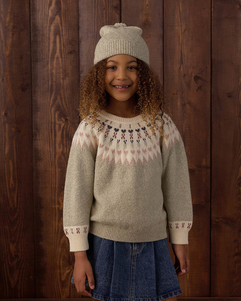A young girl wearing a beige knit sweater with a pink and dark blue Fair Isle yoke pattern