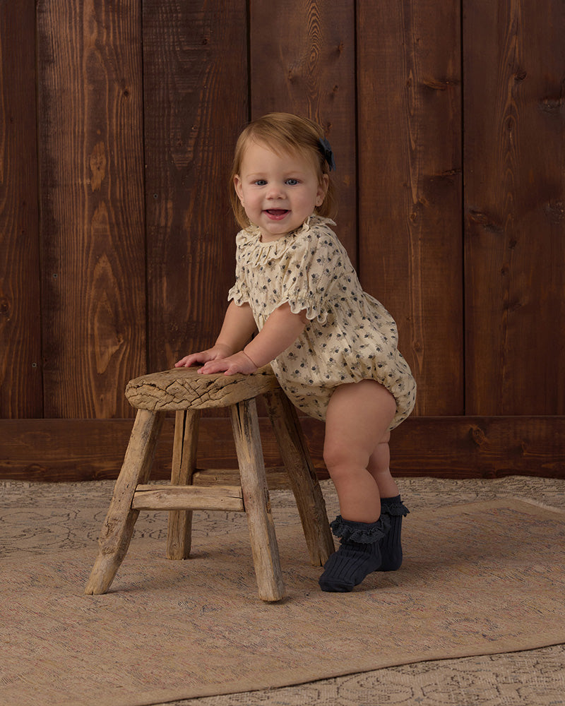 Baby romper with floral pattern and a ruffled collar and sleeves on a white background
