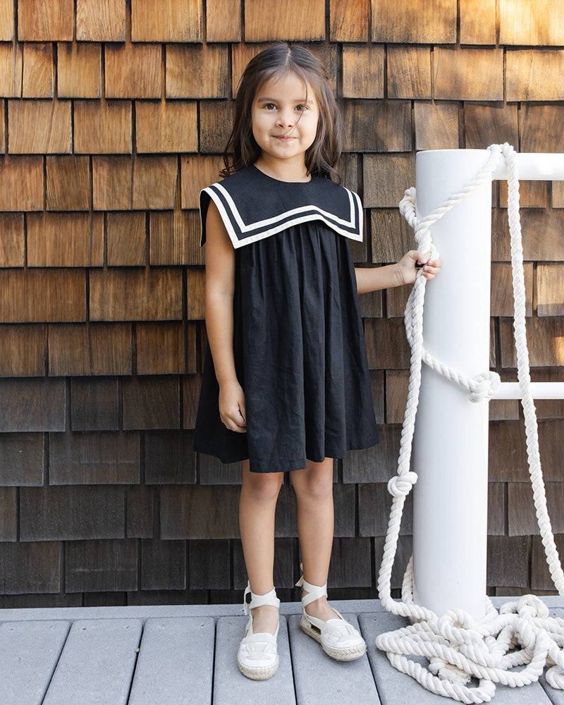 Young girl in a black dress with a square neck design and white trim