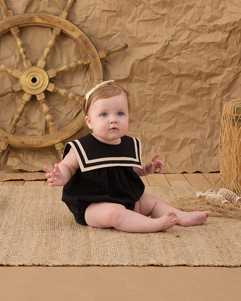 Baby in a black and white romper with a sail-style collar and a square neckline.