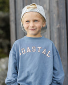 Child wearing a blue sweatshirt with 'COASTAL' text outdoors.
