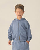 Child wearing a light blue hoodie and pants set on a beige background