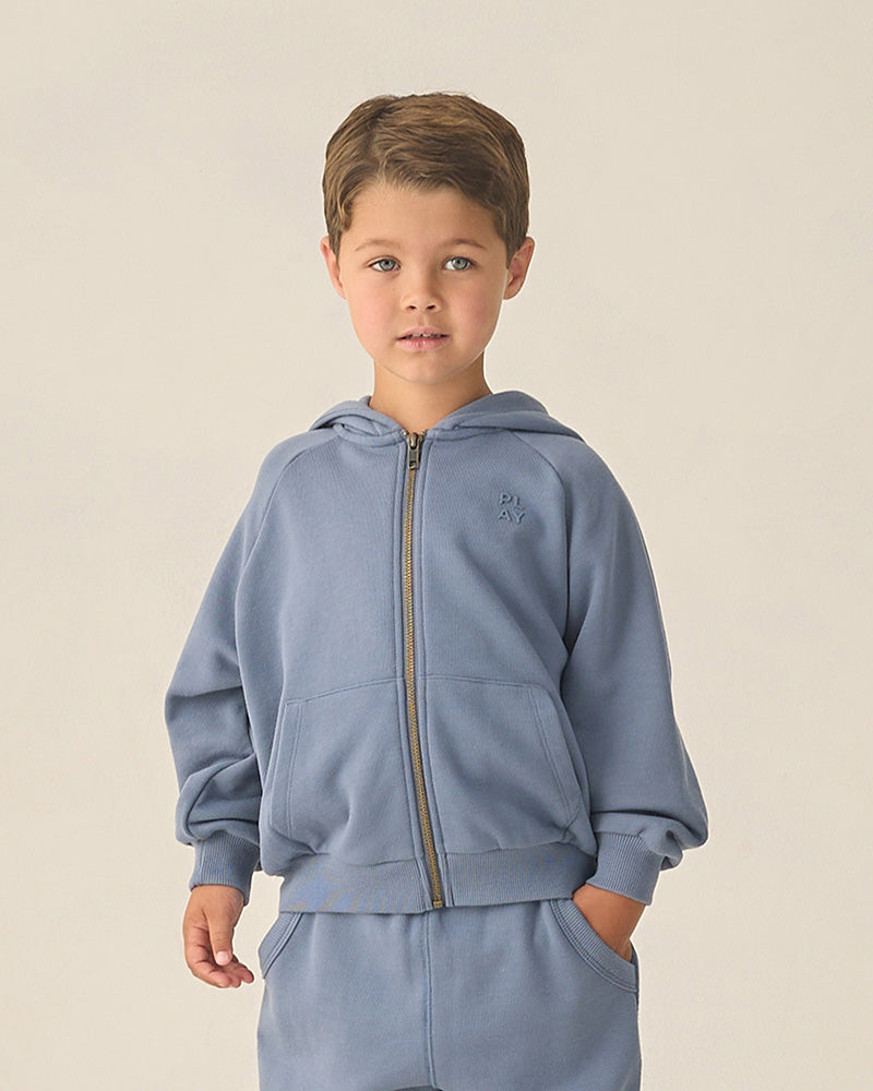 Child wearing a light blue hoodie and pants set on a beige background
