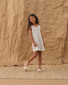 Young girl in a blue and white striped dress standing against a textured brown backdrop 