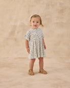 Young child wearing a blue and beige floral dress against a beige background