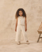 Young girl in a beige outfit standing against a beige background