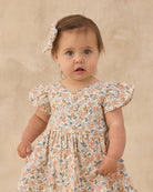 Baby wearing a floral dress against a beige background