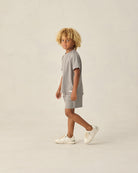 Child wearing a gray outfit with white sneakers on a beige background