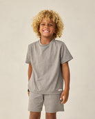 Child wearing a gray t-shirt and shorts set on a beige background