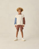 Child wearing a color-blocked sweater and shorts on a plain background