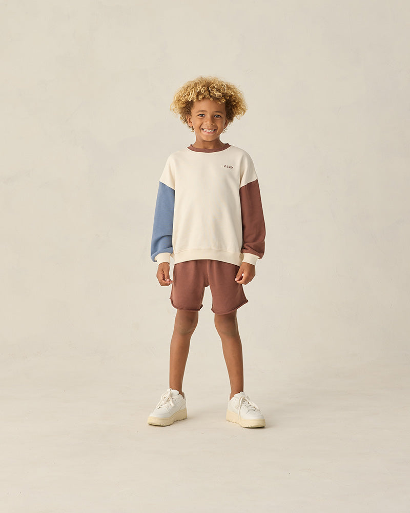 Child wearing a color-blocked sweater and shorts on a plain background