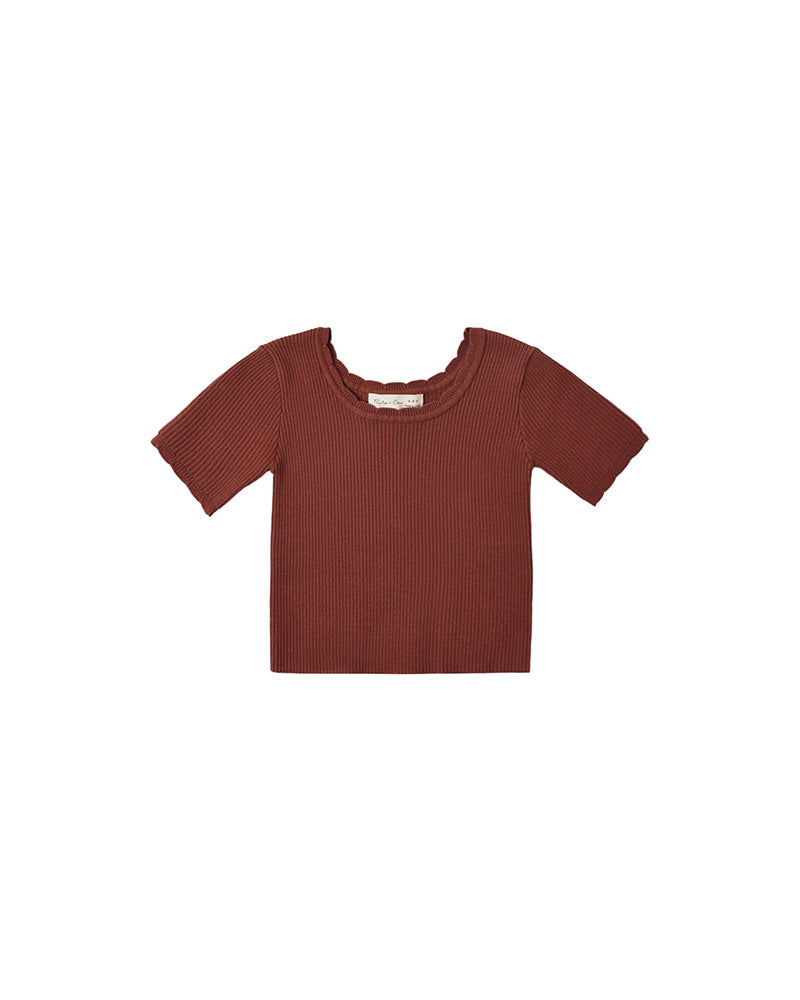 A short-sleeve ribbed knit top in a muted rust red color, with a scalloped neckline displayed flat against a solid white background.