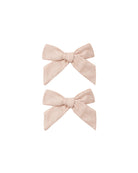 Two small bow hair clips in a light blush pink linen-like fabric.