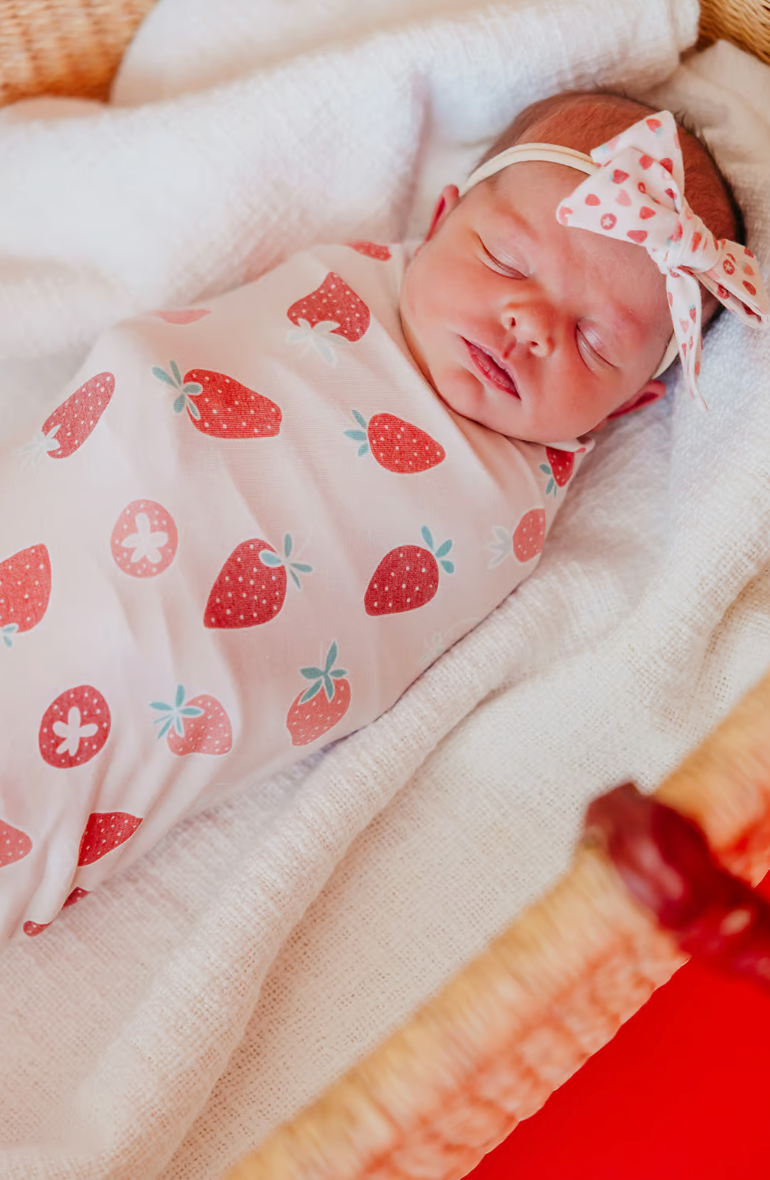 baby in strawberry print swaddle blanket with matching headband 