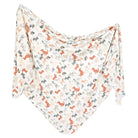 A knit swaddle blanket with a pattern of dogs, predominantly in a beige color with accents in gray and orange.