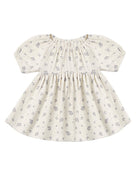 A baby girl's short-sleeve dress in cream cotton fabric with a delicate gray floral print, featuring a smocked bodice and puffed sleeves.