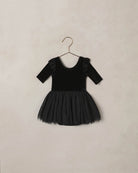 Black velvet dress with tulle skirt and a ruffle shoulder detail on a beige background