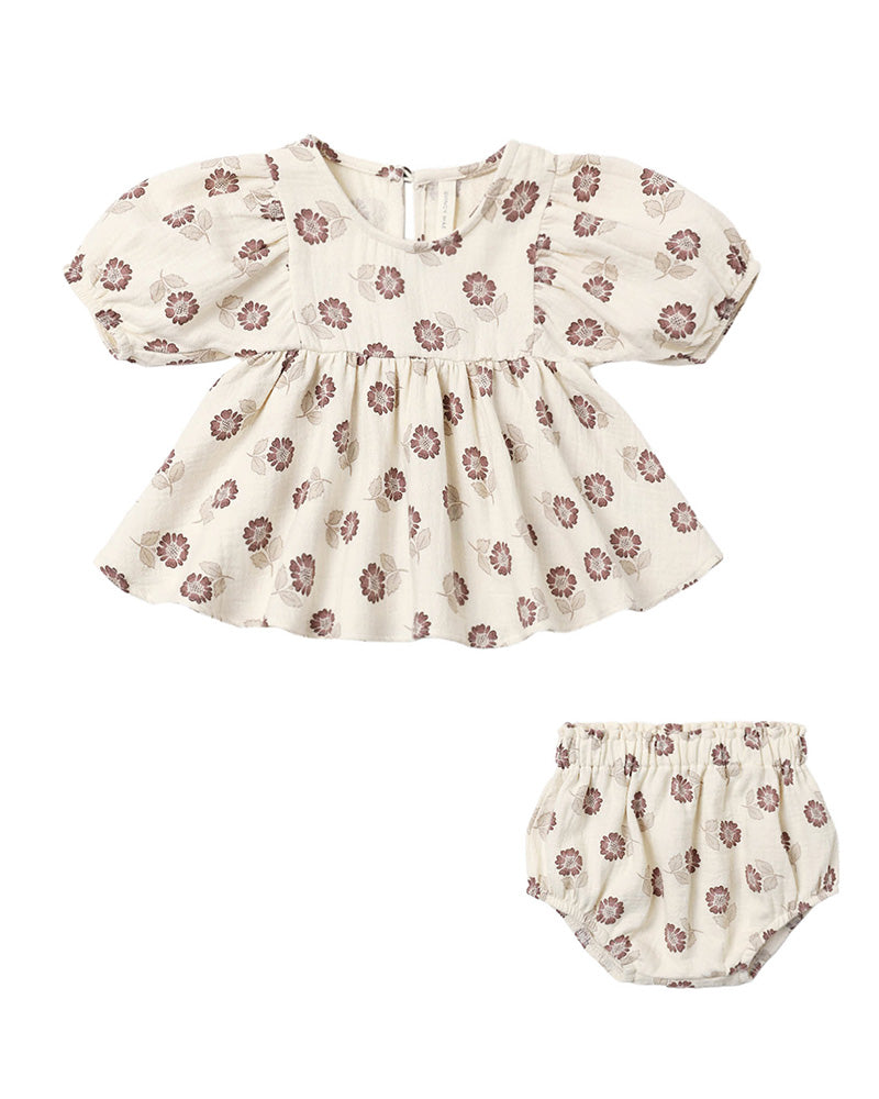 A baby girl's two-piece outfit set featuring a short-sleeve smocked blouse with puff sleeves and a matching bloomers diaper cover, both in an off-white fabric with a brown floral pattern, shown on a plain white background.