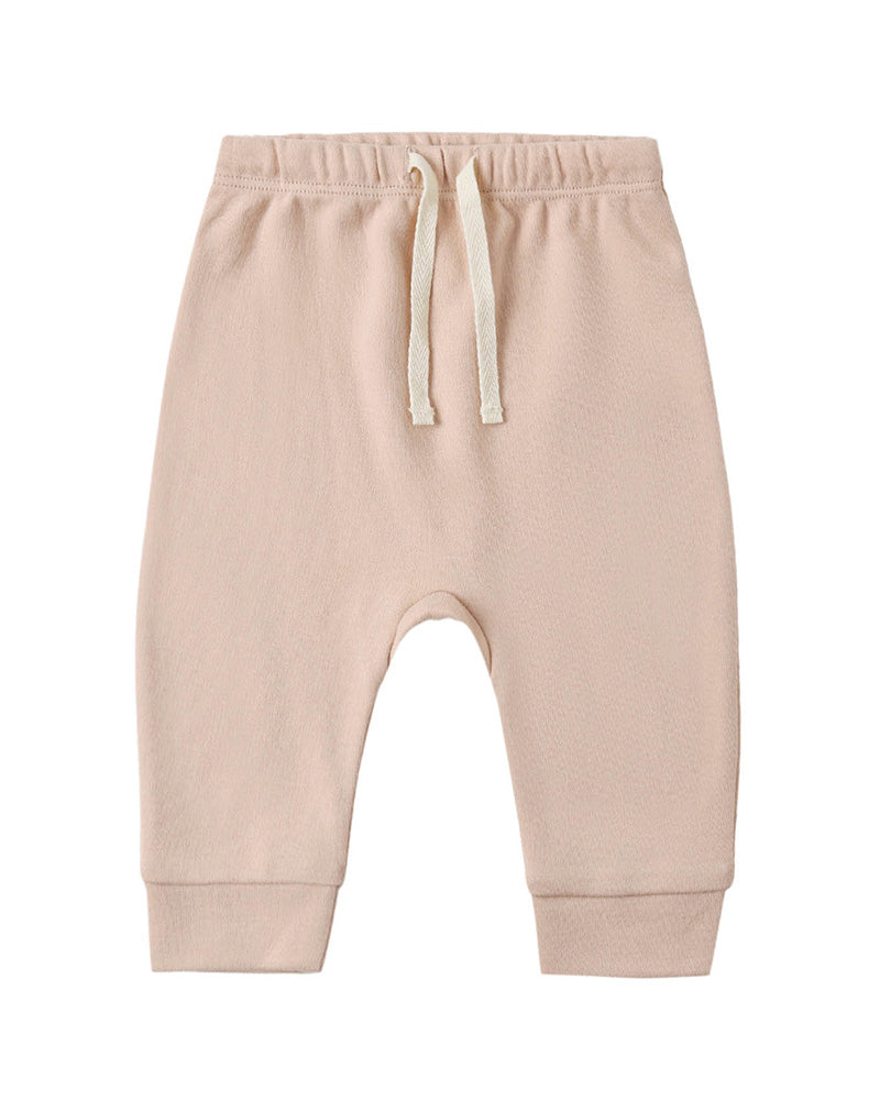 A pair of baby jogger pants in a soft, light peach-beige color, featuring an elastic waistband with a cream-colored drawstring and ribbed ankle cuffs, shown against a plain white background.