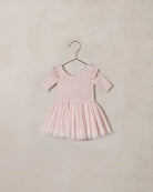 Pink dress with ruffled sleeves and a tulle skirt against a beige background