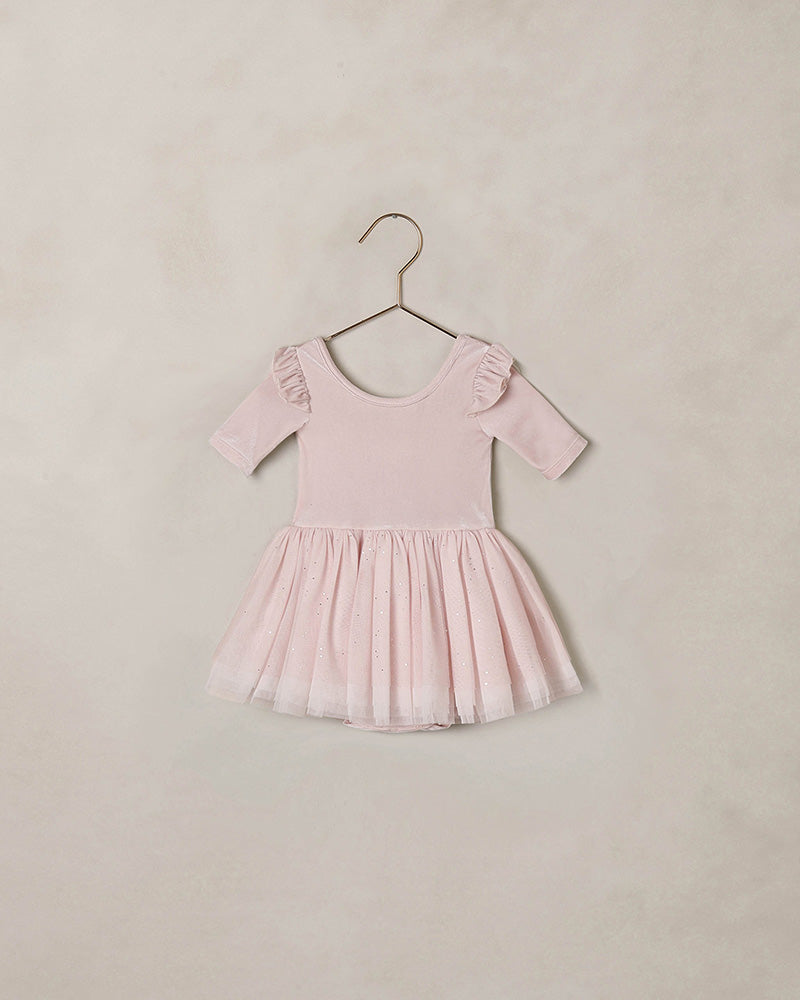 Pink dress with ruffled sleeves and a tulle skirt against a beige background