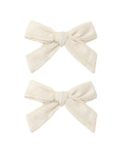 Two cream-colored hair bows on a white background