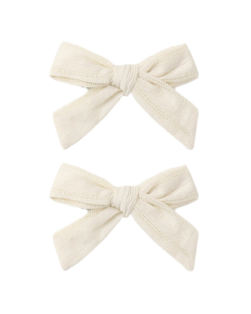 Two cream-colored hair bows on a white background